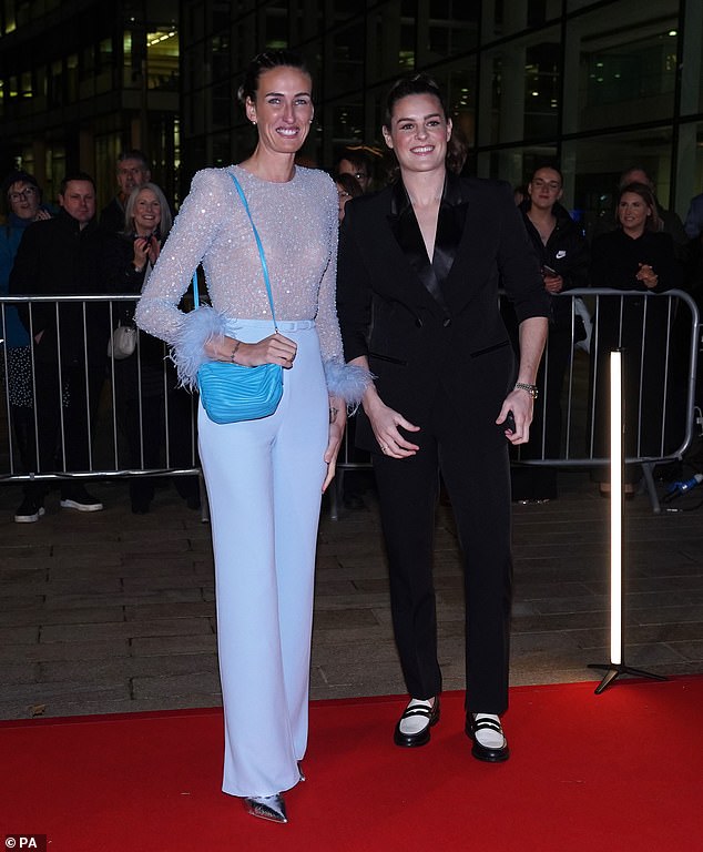 Hill paired her sheer top with light blue trousers as she beamed alongside her Scottish footballer girlfriend Jen Beattie (right)