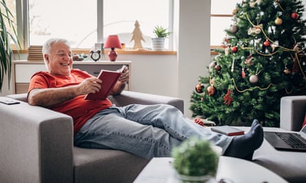 Older man reads a book near the Christmas tree at home