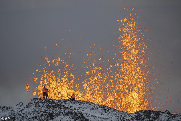 Scientists from the University of Iceland take measurements and samples while standing on the ridge in front of the active part of the erupting fissure of an active volcano in Iceland