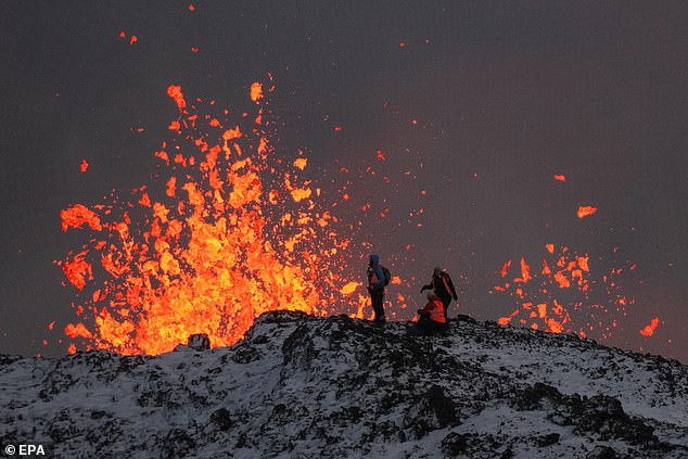 A team of scientists work at the edge of a volcanic fissure as lava spews out during a volcanic eruption