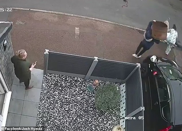 A neighbor tries to help by throwing a metal planter shaped like an oil barrel at the beige dog and hitting him on the back, but it seems to have little impact