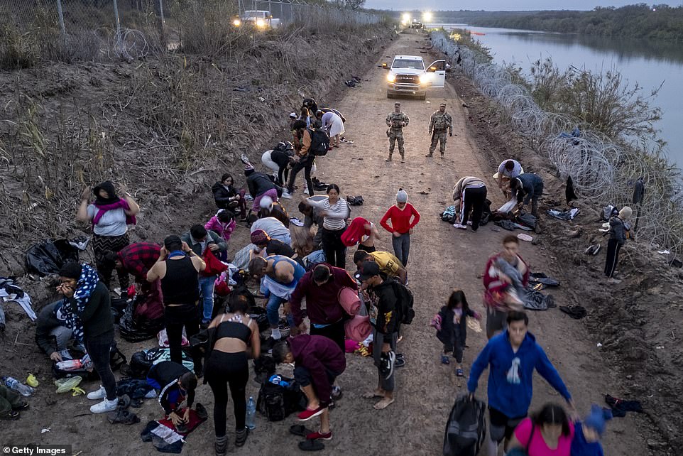 Viewed from the air, Texas National Guard troops monitor as immigrants change into dry clothes after wading through the Rio Grande from Mexico early Dec. 20, 2023, in Eagle Pass, Texas