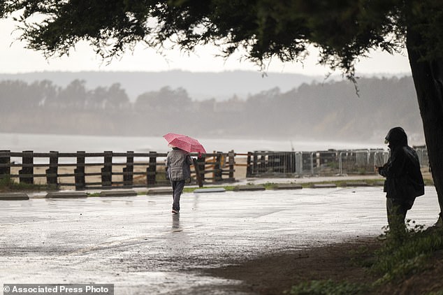 People walk through wet conditions along Seacliff State Beach in Aptos, California on Wednesday, December 20, 2023