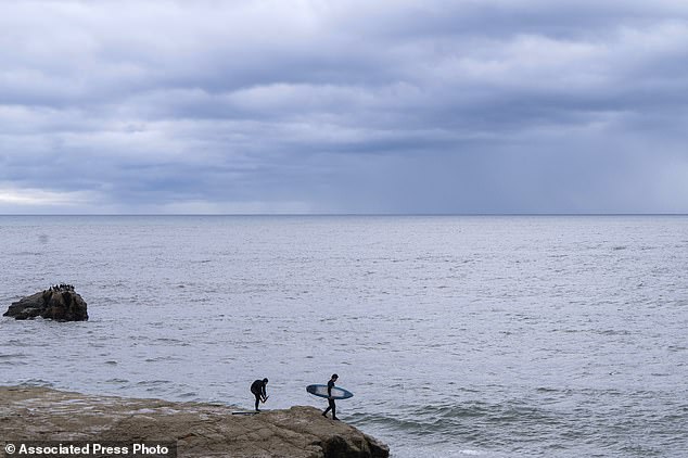 A surfer jumps into the water near Steamer Lane as storm clouds approach in Santa Cruz, California on Wednesday, December 20, 2023