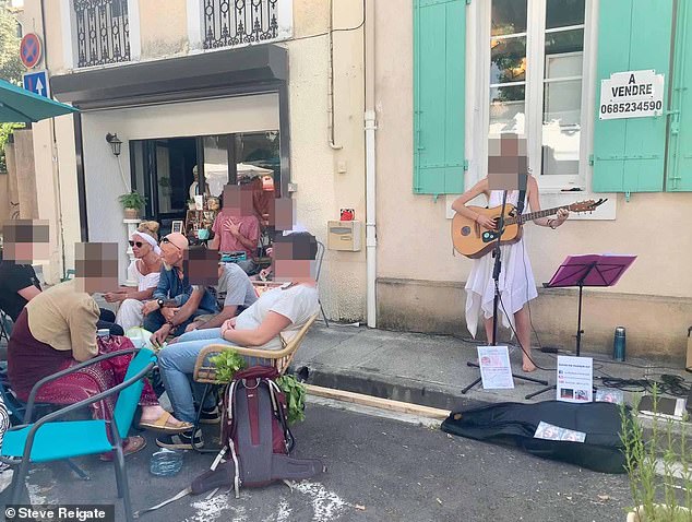 Behind the British family, a street performer plays her guitar and sings to the tourists