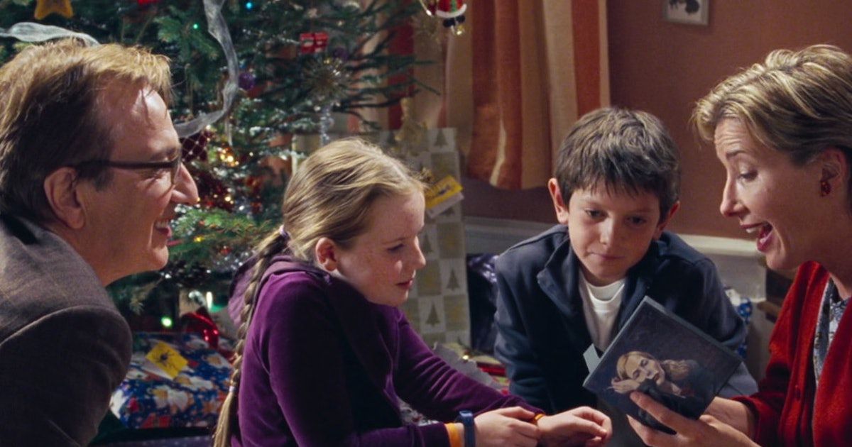 Alan Rickman watches as Emma Thompson opens a CD, while their children watch.  there is a Christmas tree in the background