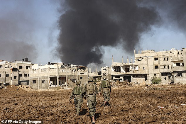 Israeli soldiers walk next to damaged buildings as smoke rises during a military operation in the northern Gaza Strip