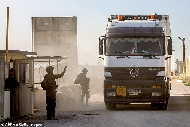 Israeli soldiers stand guard as trucks carrying humanitarian aid drive on the Israeli side of the Kerem Shalom border crossing with the southern Gaza Strip