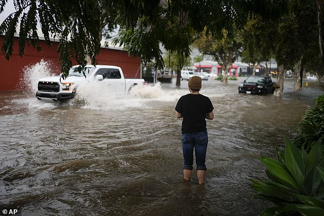 A man sees motorists driving through a flooded street during a rain shower