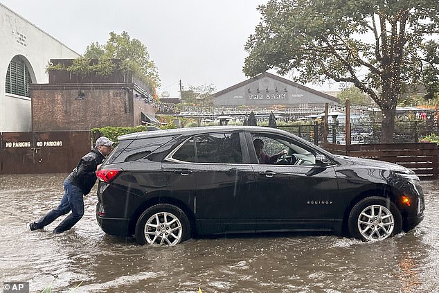 A man tries to push a vehicle out of a flooded street as it rains in Santa Barbara