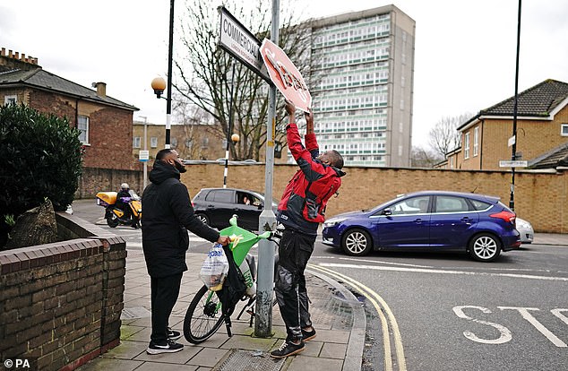 One of the men, wearing a red jacket and apparently work clothes, pulls down the sign while the second watches