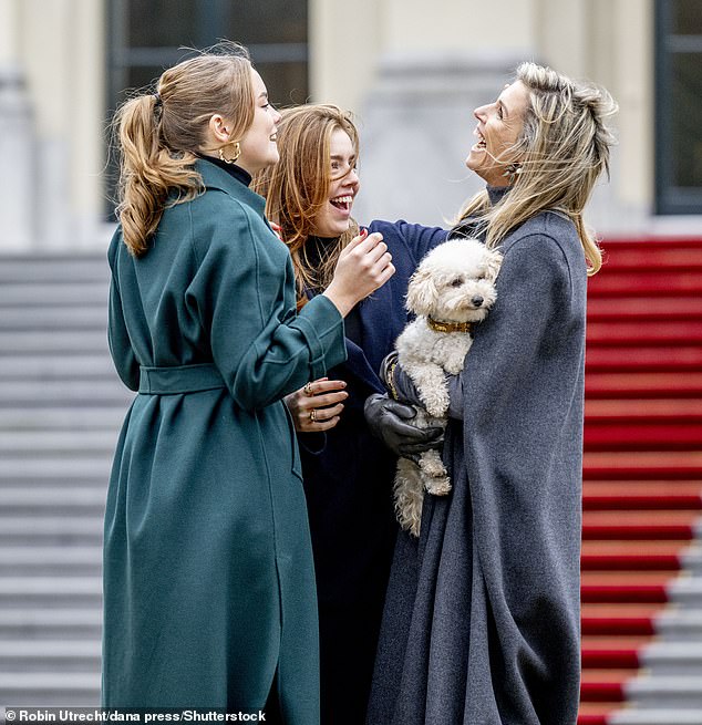 With Mambo against her chest, Queen Máxima laughed as a gust of wind caught her while Ariane and Alexia styled her hair