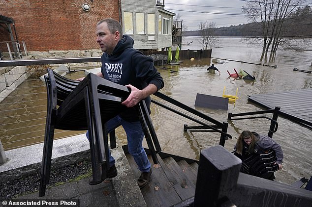 Heavy rains on the East Coast have killed at least seven people, with deaths reported in Pennsylvania, New York, Massachusetts and Maine.  Pictured: A resident of Hallowell, Maine.  wades through the floodwaters to retrieve items.