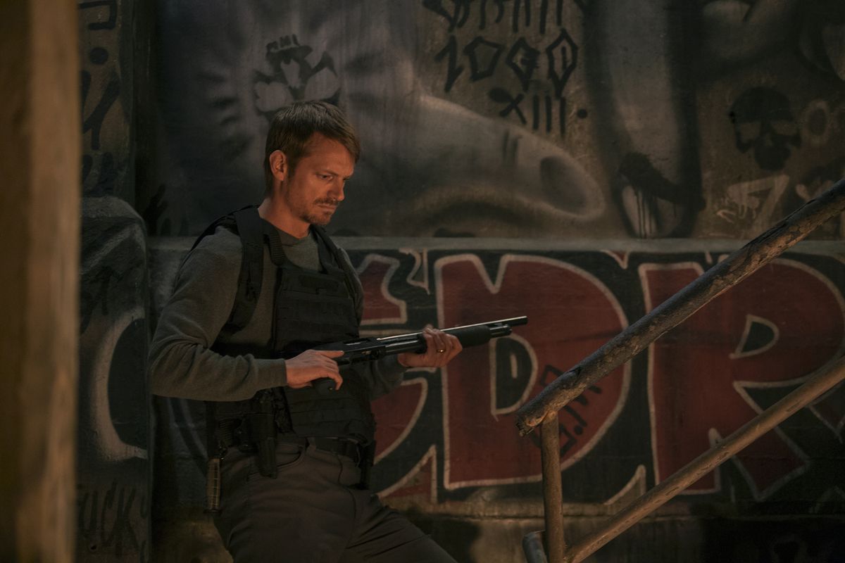 Joel Kinnaman, dressed in body armor and carrying a shotgun, prepares to climb a flight of stairs in Silent Night.