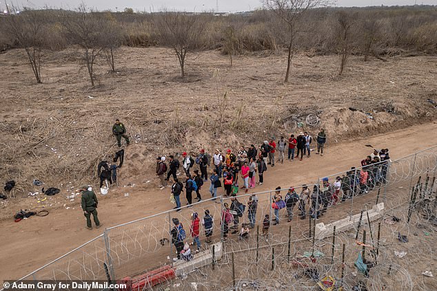 Migrants are lined up by border patrol on the banks of the Rio Grande after crossing the border into Eagle Pass