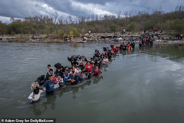 A convoy of migrants wades across the Rio Grande near Eagle Pass, carrying everything they have above water