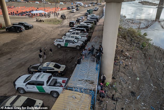 Aerial view of migrants climbing over shipping containers and barbed wire in Eagle Pass after crossing the Rio Grande