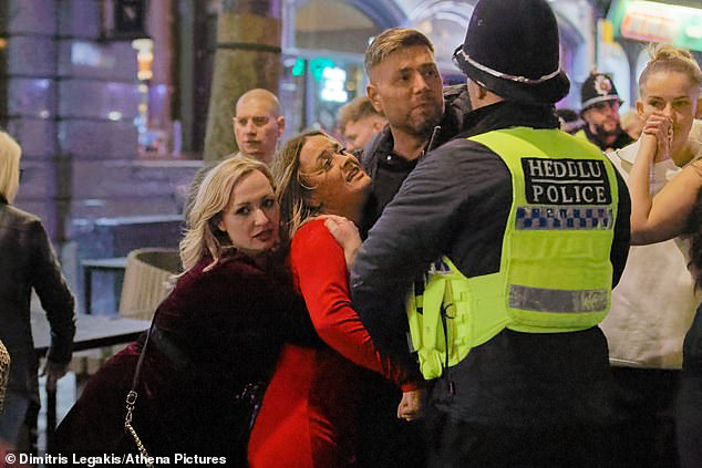 The third photo shows a man and a woman arguing with a police officer in the hectic street, while another woman lovingly embraces them