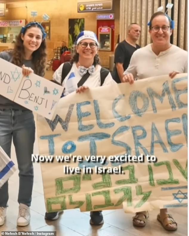 People gather at the airport, holding up welcome signs and Israeli flags for the newcomers