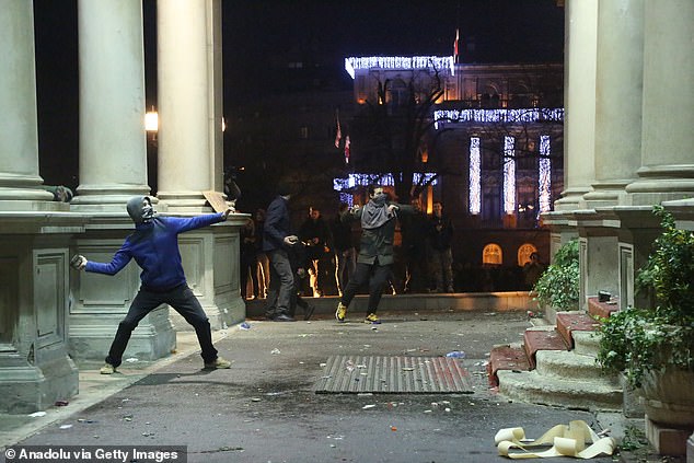 Pictured: Protesters throw stones at Serbia's city council building amid unrest after last weekend's elections