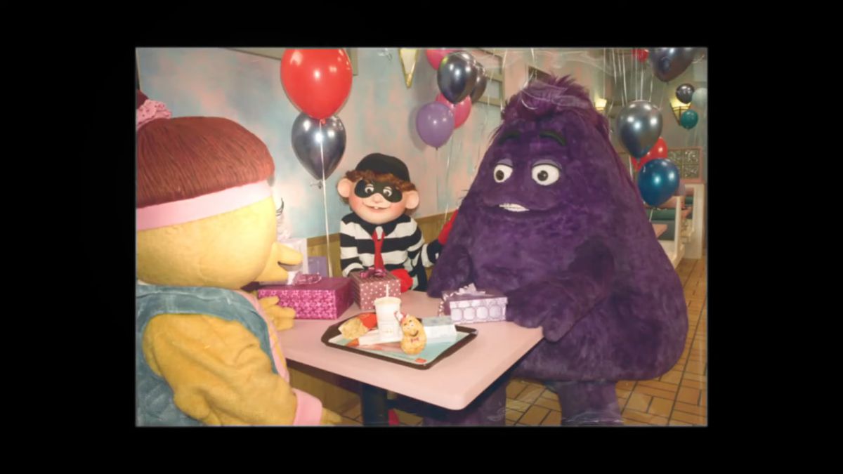 An old photo of Grimace, the Hamburgler, and a Birdie and Early Bird sitting around a table eating McDonald's.