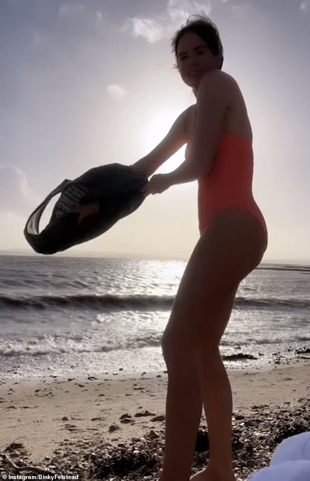 Binky could be seen taking off her top to reveal a bright orange swimsuit as she stood on the beach