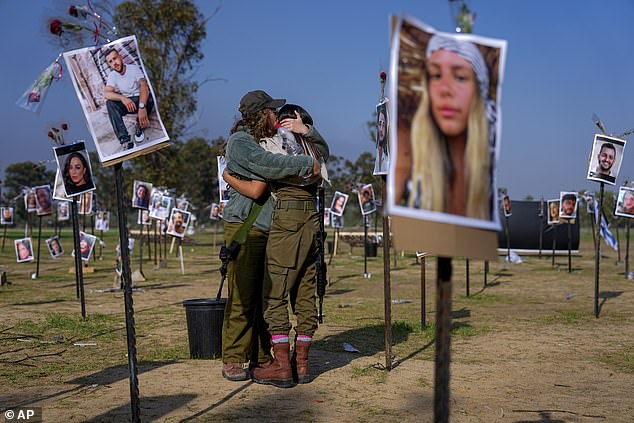 Israeli soldiers hug each other next to photos of people killed and captured by Hamas militants during their violent rampage at the Nova music festival in southern Israel, which are on display at the site of the event, commemorating the October 7 massacre , near kibbutz Re'im, Friday December 1, 2023