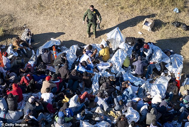 A U.S. Border Patrol agent speaks with immigrants awaiting processing after crossing into the United States from Mexico on December 17