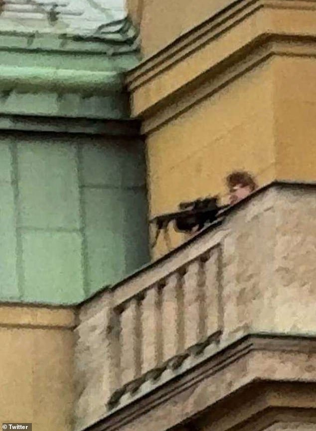 A chilling image shows Kozak, dressed in black, pointing a gun at people below as he stands atop a faculty building