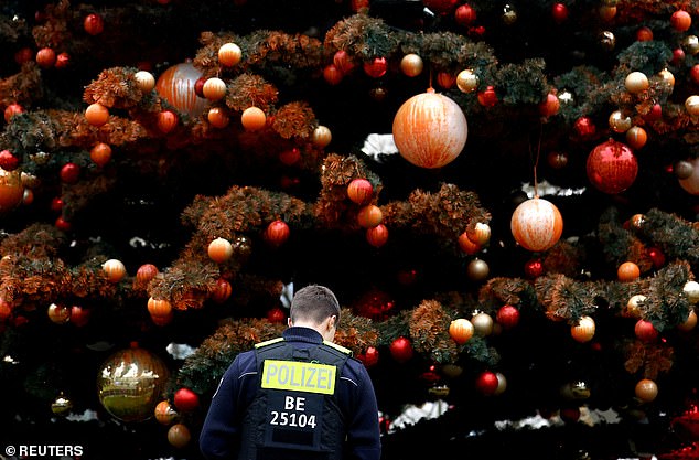 A police officer in Berlin inspects a Christmas tree after climate change activists from the group Letzte Generation, funded by a Californian climate group, sprayed it with orange paint