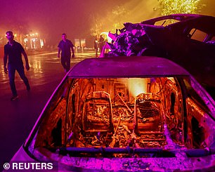 People walk near burned-out cars that have been recovered from the scene