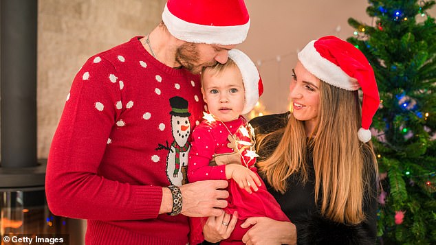 A young couple holds their baby tightly on Christmas Day as they dress in festive sweaters (stock image)