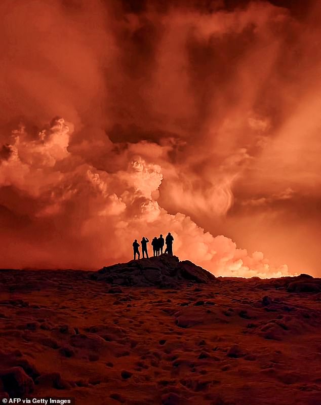 Local residents see smoke rising as lava turns the night sky orange after a volcanic eruption on the Reykjanes Peninsula