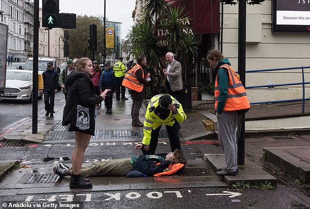 A JSO activist lies at an intersection near Earl's Court as police try to move her