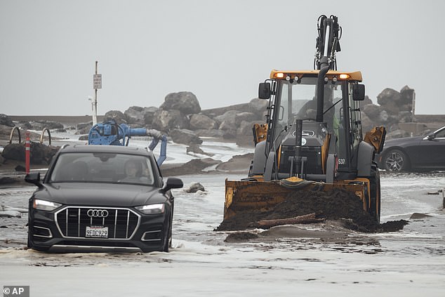 Construction vehicles are seen clearing debris as a black Audi tries to make its way through flooded streets in Pacifica