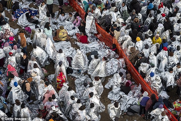 In this aerial view, immigrants, many wearing mylar blankets provided by the U.S. Border Patrol, try to stay warm after spending the night outside a processing center near the U.S.-Mexico border on December 18, 2023
