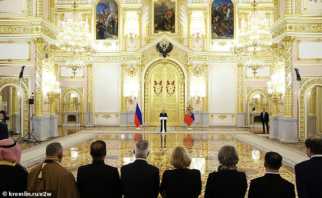 Putin could be seen speaking confidently as he stood an uncomfortable distance from the ambassadors in front of a huge golden door with flags on either side of him