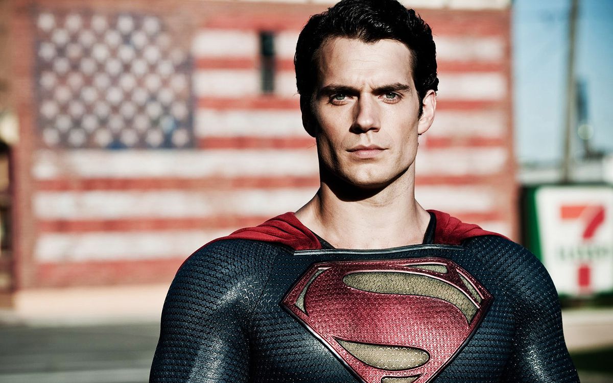 Henry Cavill as Superman standing in front of a mural of the American flag in the background in Man of Steel.