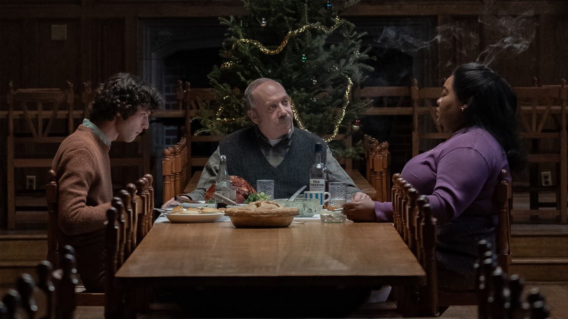 Dominic Sessa, Paul Giamatti and Da'Vine Joy Randolph gather around a table with a Christmas tree in the background in The Holdovers.