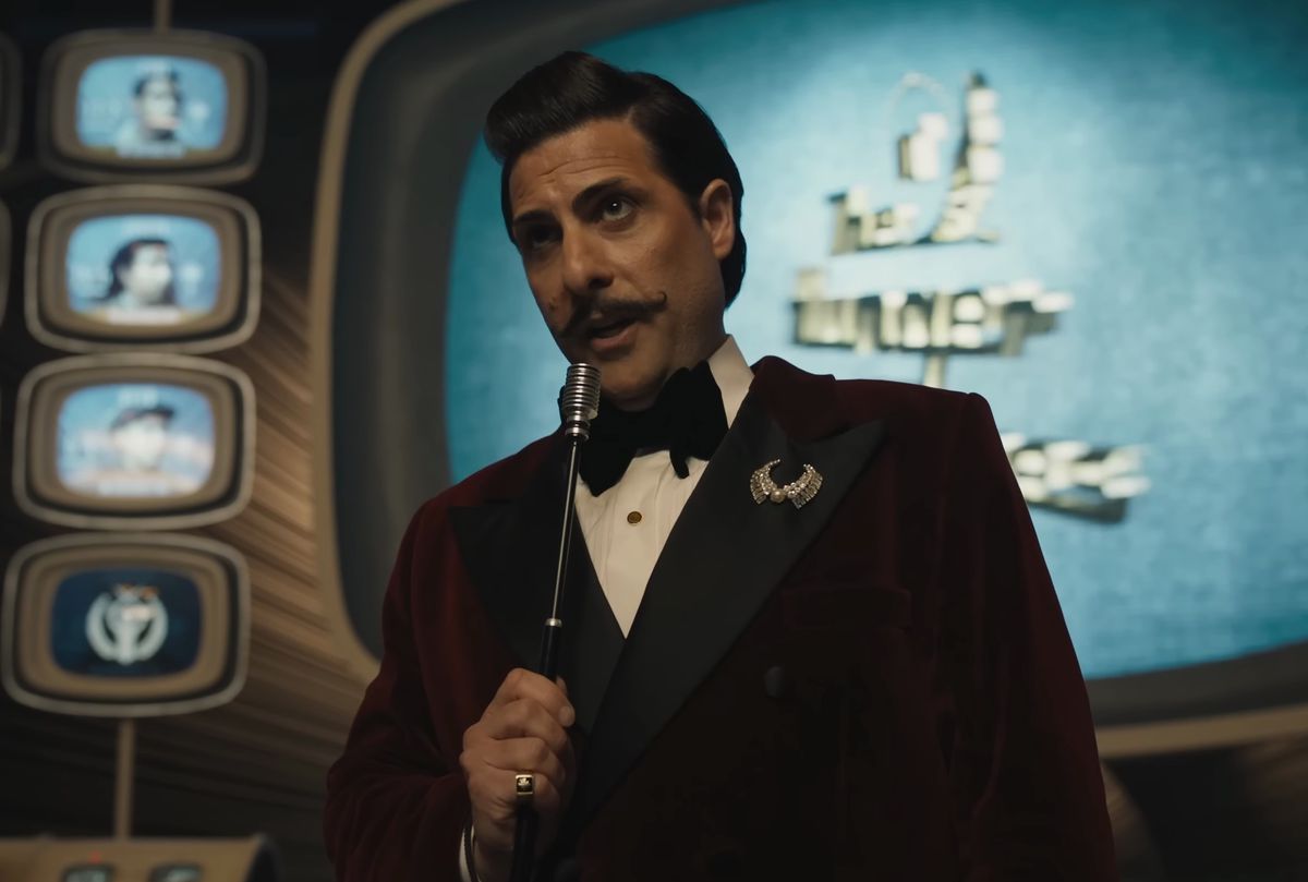 Jason Schwartzman with handlebar mustache plays Lucky Flickerman and holds a microphone for Hunger Games TV in The Ballad of Songbirds and Snakes