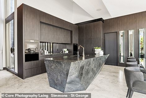 The sleek kitchen in the split-level family room features a geometric gray marble island bench and a mirror back wall