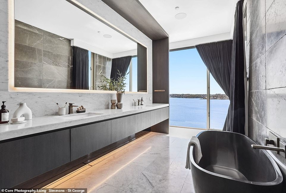 The chic bathroom has a double sink and a freestanding black bath with floor-to-ceiling windows offering a glimpse of the beautiful landscape