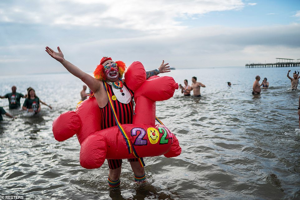 A reveler smiles big as he stands in the ocean water, dressed as a clown and surrounded by a red float in the shape of a dog, marking the New Year at Brooklyn's Coney Island event