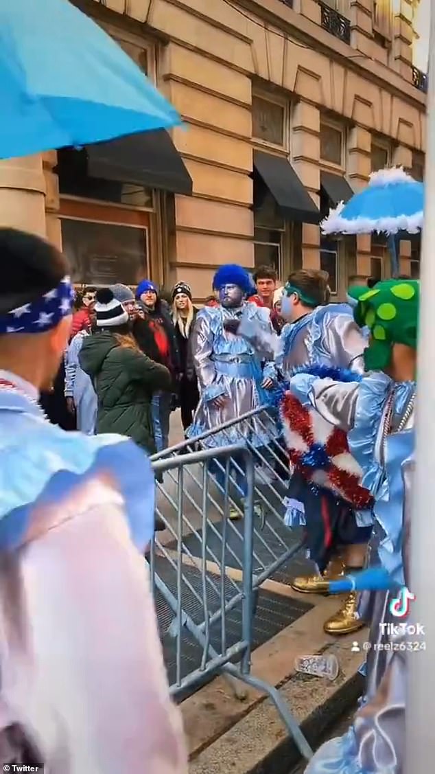 The video shows the spectator having a heated argument with the parade participant as another member of his group gathers around him