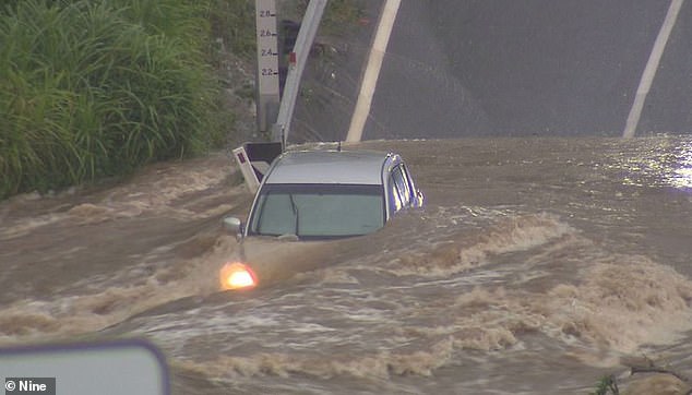 Images shared on social media showed a Queensland driver stranded and sitting on the roof of his car surrounded by floodwaters (pictured)