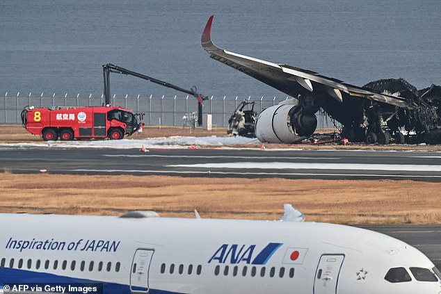 An All Nippon Airlines (ANA) plane passes the burned wreckage of the Japan Airlines (JAL) plane on the tarmac the day after the collision