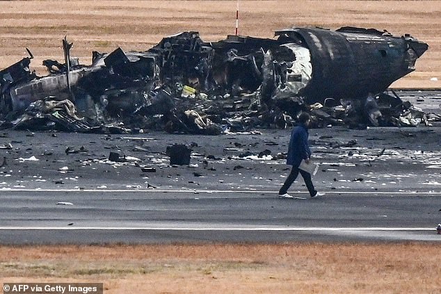 An official views the wreckage of a Japanese Coast Guard plane on the tarmac of Tokyo International Airport in Haneda.  The disaster is being investigated