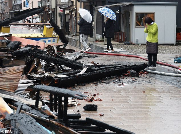 A woman prays at the remains of a building burned down by a fire that followed the strong earthquake in Wajima, central Japan