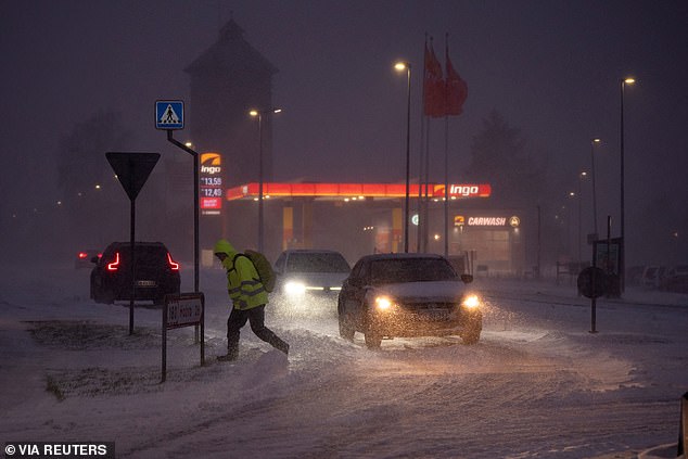 Vehicles drive next to a pedestrian amid heavy snowfall in Randers, Denmark, January 3