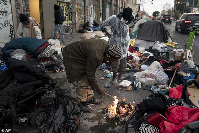 Robert Mason, a 56-year-old homeless man, warms a piece of donut over a bonfire he lit to keep himself warm on Skid Row in Los Angeles, on February 14, 2023